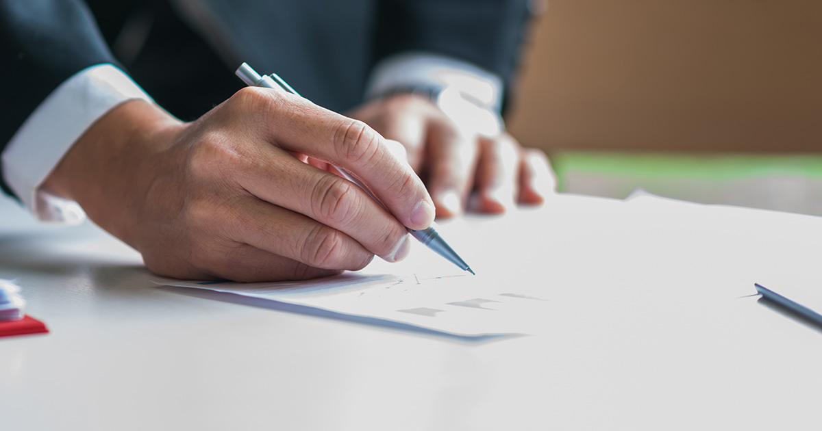 Nahaufnahme: Ein Geschäftsmann hält einen Stift bereit, um ein Dokument zu unterschreiben.