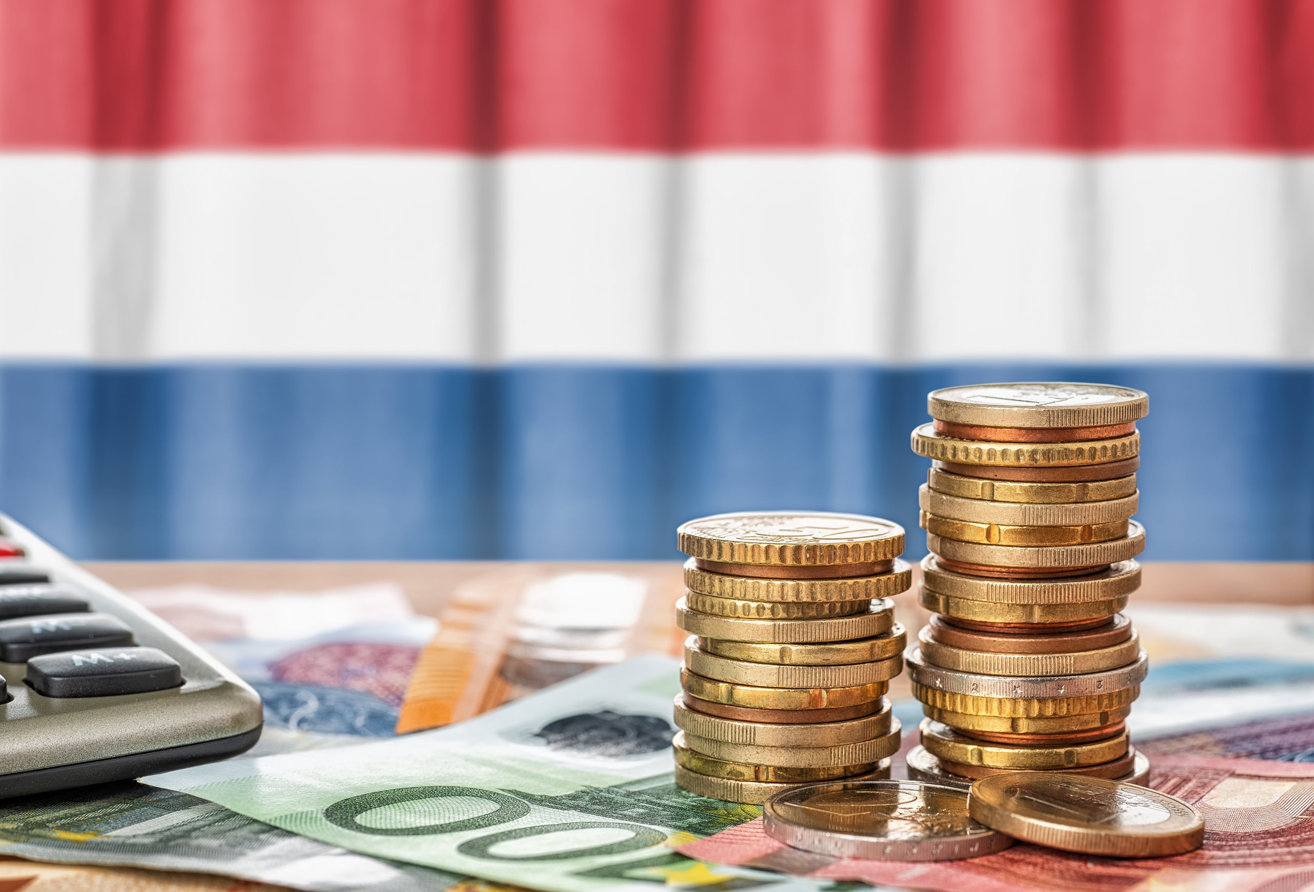 Banknotes and coins in front of the national flag of the Netherlands